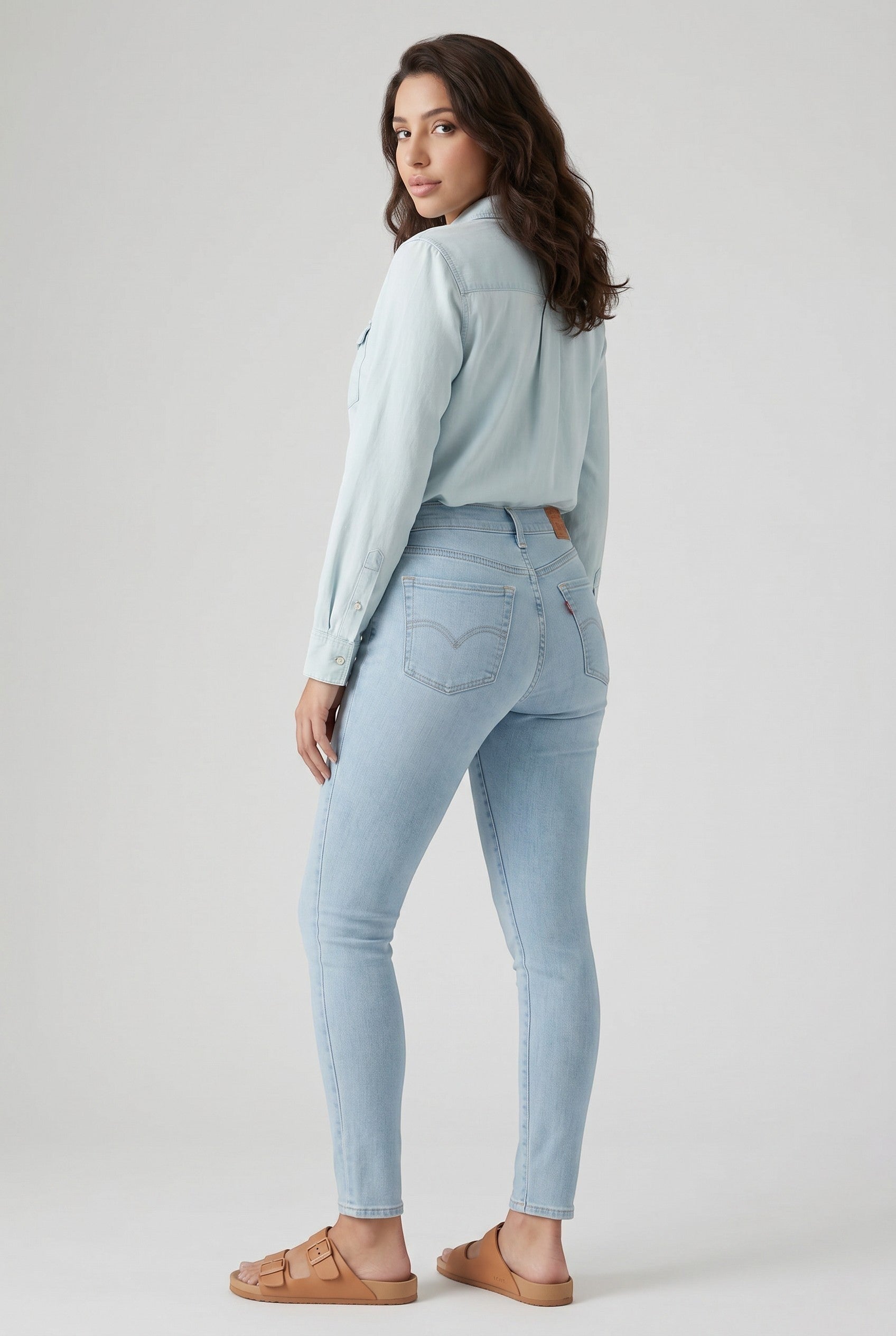 Vella Moda model wearing Levi's 711 light wash skinny jeans and a denim shirt with tan sandals, back view