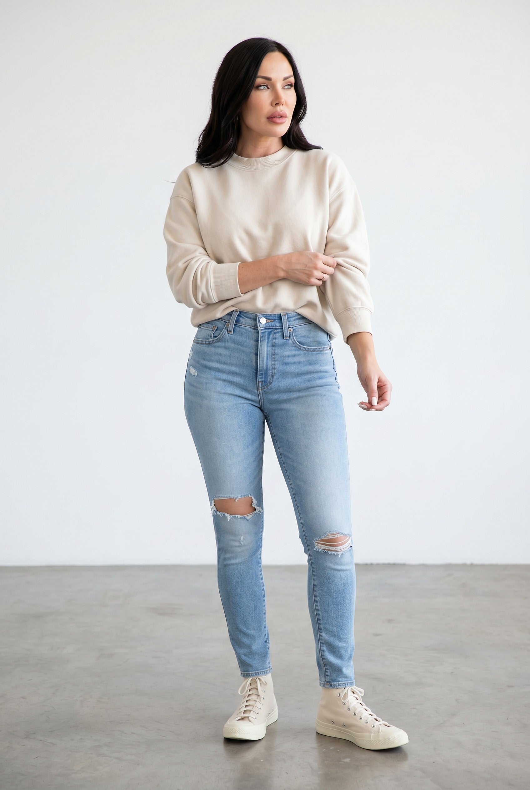 Woman wearing a beige sweater and light blue jeans with a white background