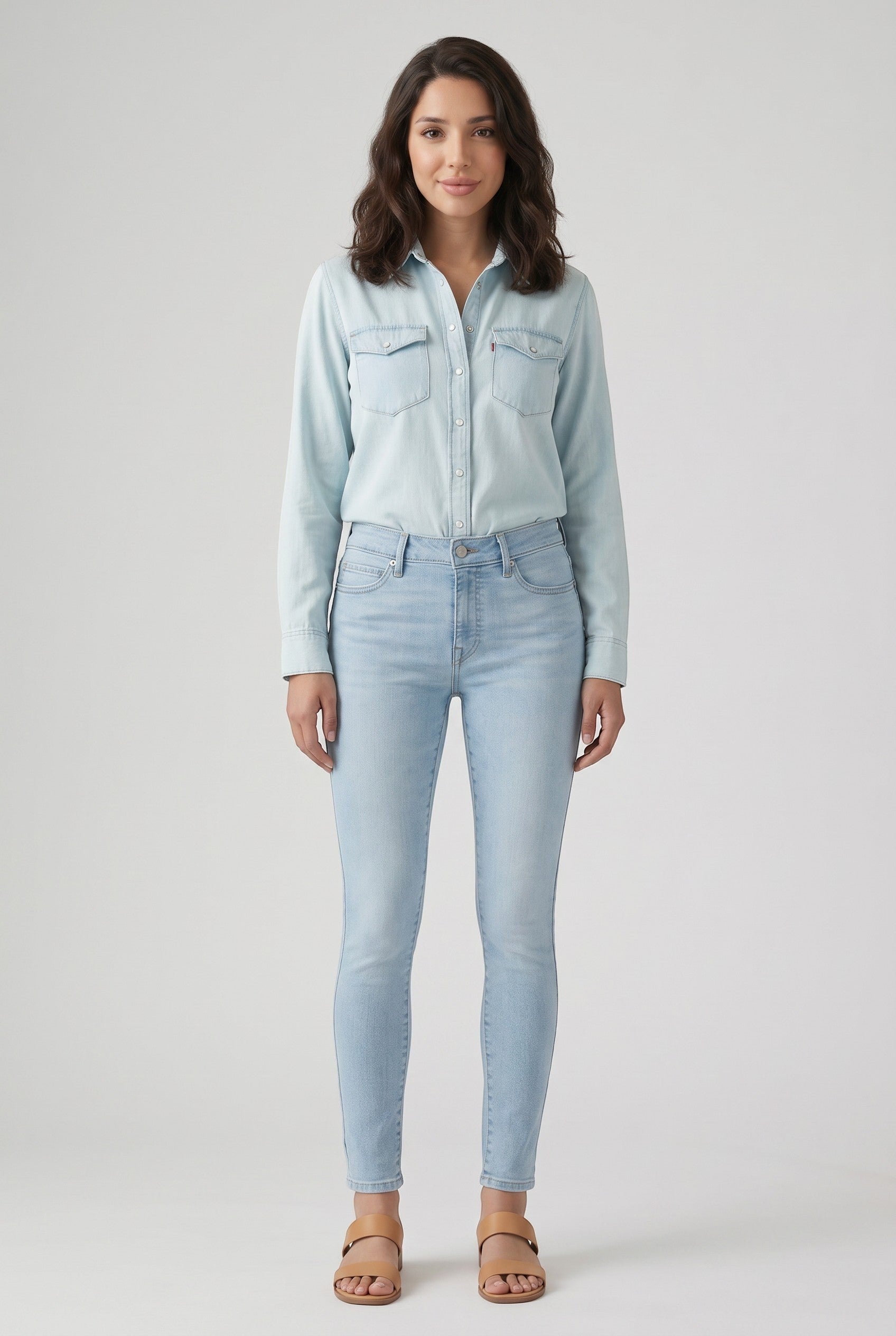Vella Moda model wearing Levi's 711 light wash skinny jeans and a matching denim shirt with tan sandals