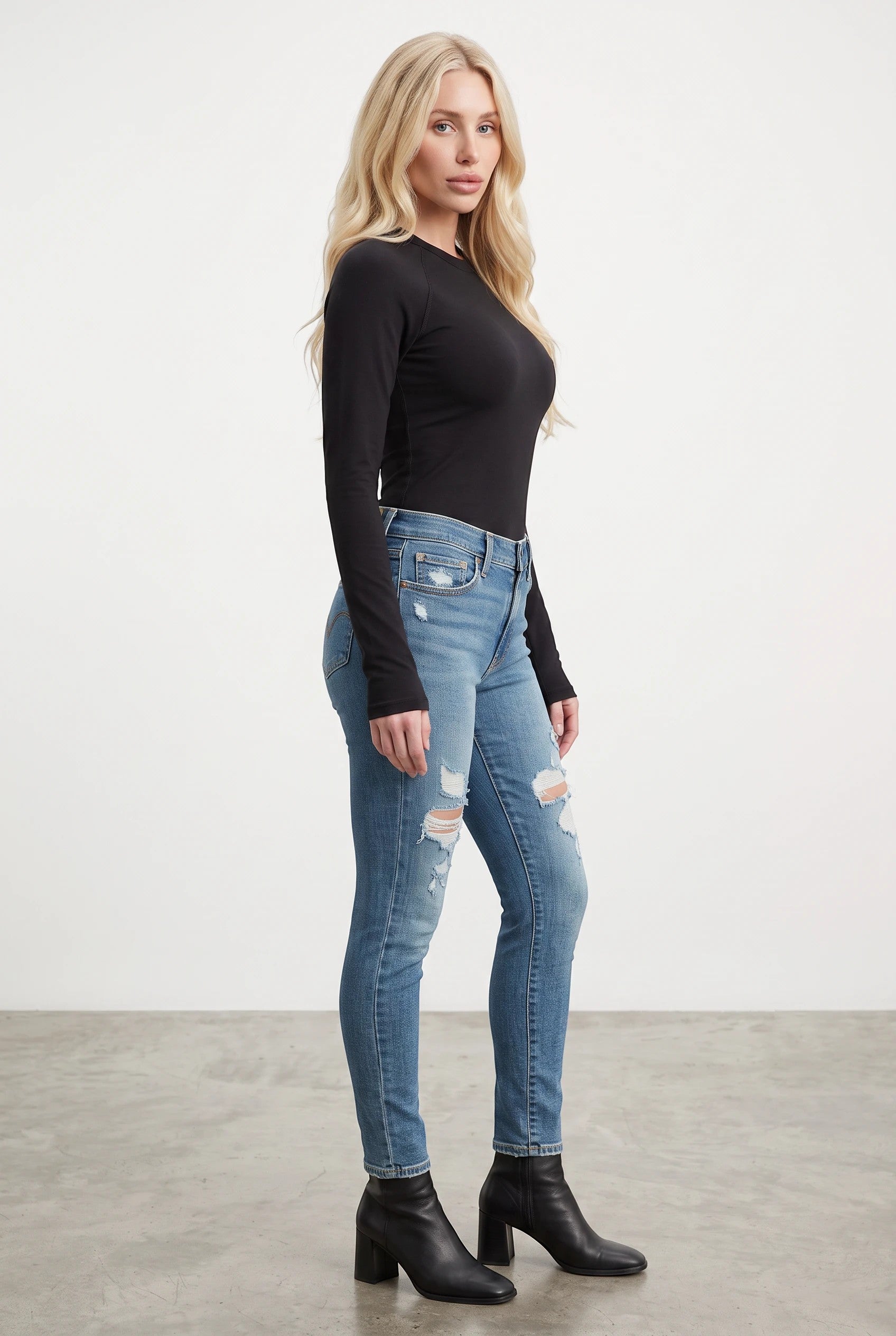 Vella Moda model wearing Levi's 711 mid-rise skinny jeans in medium wash with distressed knees and black ankle boots